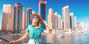 Cheerful girl traveler on a ferry boat sailing through Dubai Marina port among huge skyscrapers. Concept of tourism in the UAE